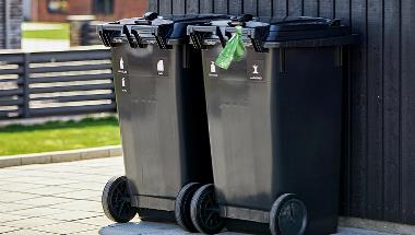 To sorte affaldsbeholder med grøn pose til madaffald bundet på håndtaget af den ene.